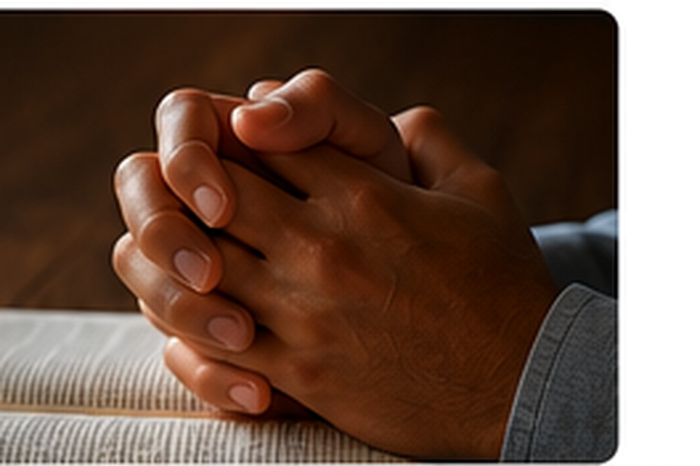 Hands folded in prayer beside an open Bible